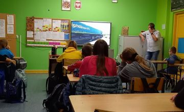 Uczniowie siedzą w klasie i oglądają prezentację. Na ekranie widać pędzący pociąg.